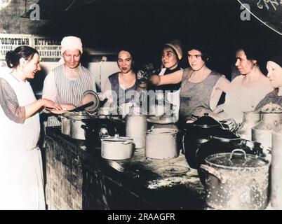 Seven women busying themselves around a stone work top adorned with an array of large tins and pots in a 1920's Russian communal kitchen.     Date: 1920's Stock Photo