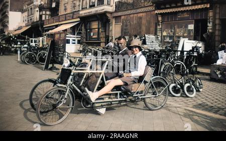 A couple on a four-wheeled two-seater cycle (also known as a velo double) outside the Taverne Emile in a town in Belgium.     Date: 1936 Stock Photo