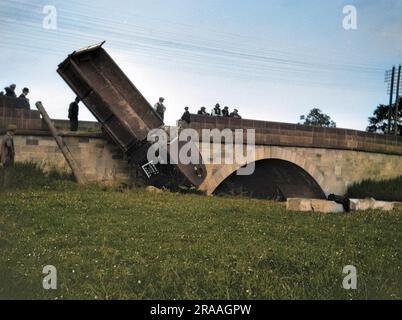 A lorry (Lewin's Lorries for Loads) which has fallen off a low bridge onto a grassy area.  People stand around looking fairly helpless.     Date: 1926 Stock Photo