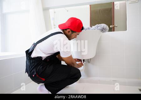 Repairman in black overalls repairing cabinet in kitchen at house, Technician examining oven with in kitchen, Maintenance and household service Stock Photo
