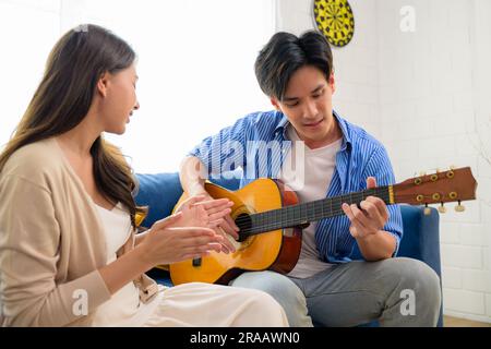 Couple of man and woman playing guitar together at home on weekend, Happy people enjoying and relaxing at home, People lifestyle, Romantic couple with Stock Photo