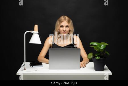 Cheerful business lady working on laptop in office. Happy blonde businesswoman work in workplace. Attractive female employee office worker smile. Stock Photo