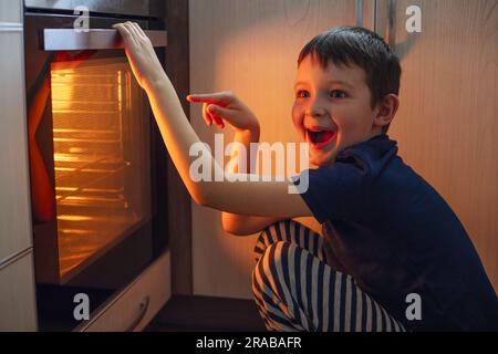 A child is sitting near the oven in the kitchen and waiting. Stock Photo