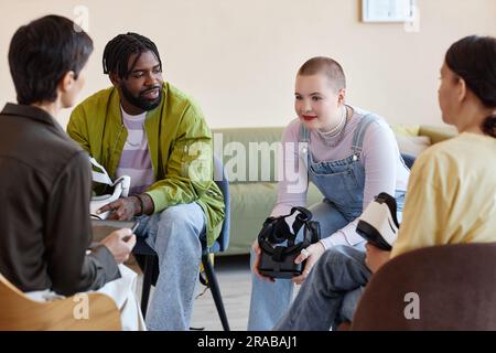 Group of young people having conversation with psychologist while testing VR glasses at session Stock Photo