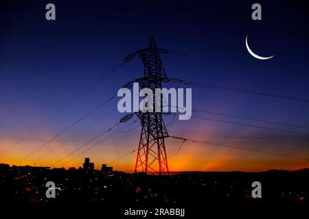 Electricity transmission tower silhouetted against blue sky at dusk Stock Photo