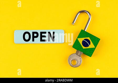 On a yellow surface, an open lock with the image of the flag of Brazil with a key and a sticker with the inscription - open Stock Photo