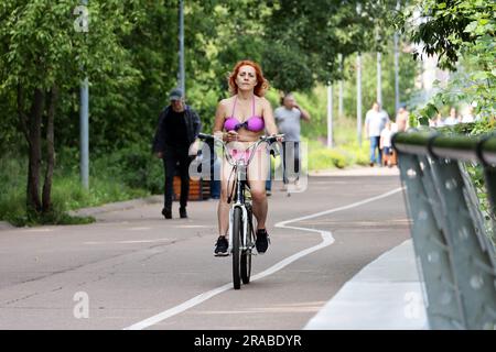 Woman in bikini riding bicycle city street. Cycling and summer leisure in hot weather Stock Photo