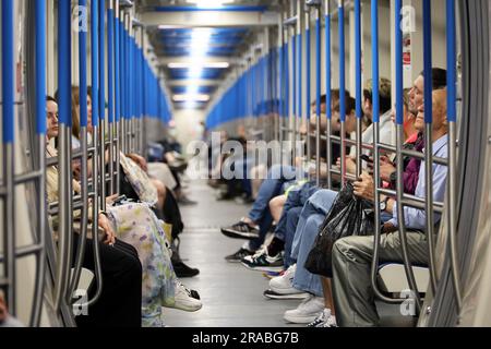 Crowd of people in a metro train in summer, passengers sits with smartphones. Interior of subway car Stock Photo