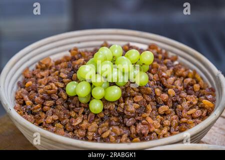 Raisins for the original Dresden Christstollen come from the light, seedless Sultana grape variety grown in Turkey or Australia. A bowl full of dark sultanas is topped with a bunch of green grapes. The photograph was taken at the Dresdner Backhaus bakery, Dresden, Saxony, Germany. Stock Photo
