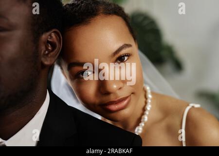 Closeup portrait of beautiful black woman as bride looking at camera over husbands shoulder Stock Photo