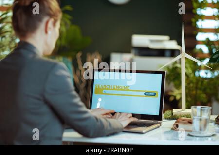 Seen from behind modern business woman with laptop using search engine in modern office. Stock Photo