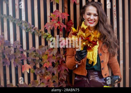 Hello november. happy elegant woman in brown trench coat with autumn yellow leaves in the city. Stock Photo