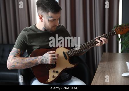 Handsome hipster man playing guitar in room Stock Photo