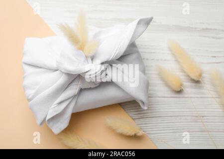 Furoshiki. Things packed in fabric and dried flowers on wooden table, flat lay Stock Photo