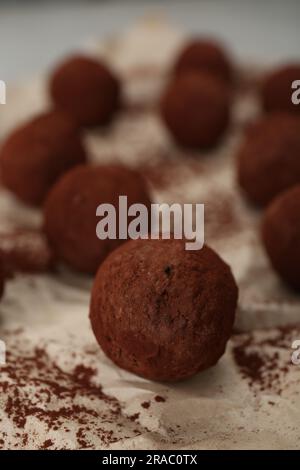 Delicious chocolate candies powdered with cocoa on parchment paper, closeup Stock Photo