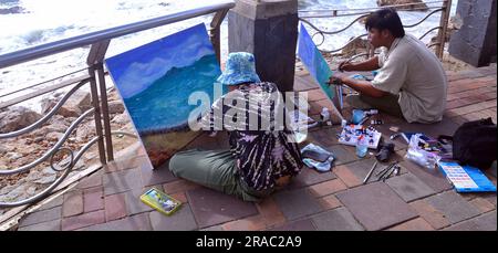 Two young men paint seascapes on canvases as they sit beside the sea in Pattaya, Thailand; painting painters art artistic theme Stock Photo