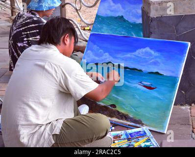 Two young men paint seascapes on canvases as they sit beside the sea in Pattaya, Thailand; painting painters art artistic theme Stock Photo