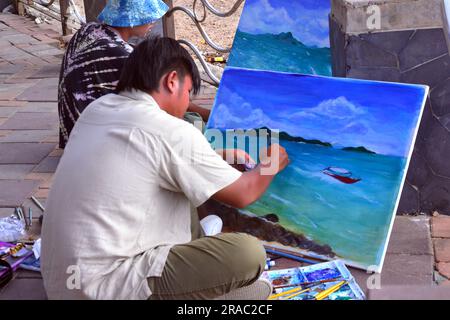 Two young men paint seascapes on canvases as they sit beside the sea in Pattaya, Thailand; painting painters art artistic theme Stock Photo