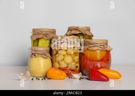 Jars with different pickled products and fresh peppers on white table Stock Photo
