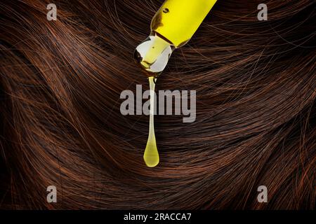Dripping cosmetic oil from pipette onto brown hair, closeup Stock Photo