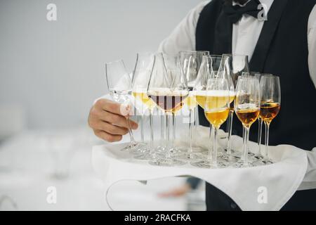 Various alcoholic beverages in different glass on tray holding wine waiter, close up. Service, serving concept. Stock Photo