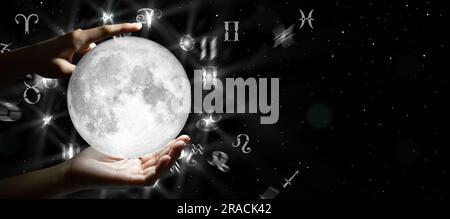 Astrological zodiac signs over the moon in hand. Knowledge of the stars in the sky. The power of the universe concept. Stock Photo