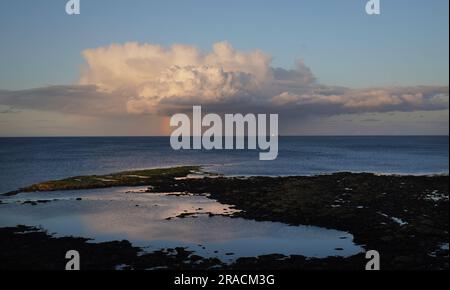 A ship sits on the horizon at sunset as a rainbow forms off the coast near Cullercoats Bay in the North East of England. Picture date: Sunday July 2, 2023. Stock Photo