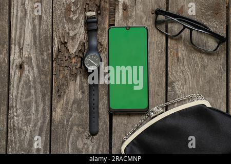 black small bag glasses watch and phone with green screen on wooden table Stock Photo