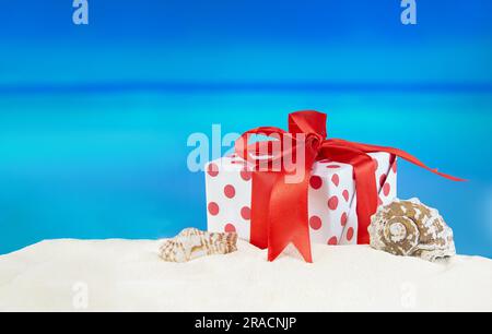 White-red gift box with polka dots with bow on sandy beach with starfish and seashell. Sale. Christmas, New Year, birthday. Holidays in hot countries. Stock Photo