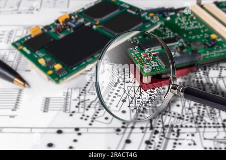Electronic modules, magnifying glass and pen on background of  schematic circuit diagram. Concept for development and design of electronic devices. Stock Photo