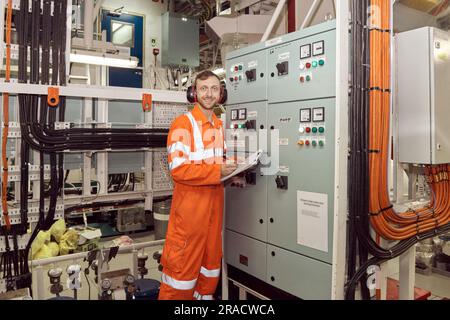 Young professional engineer checking parameters of high voltage switch board. Offshore engineer making high voltage electrical equipment checks. Stock Photo