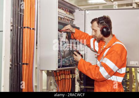 Electrician fault finding in electrical switchboard in the engine room. Young oil and gas industry professionals. Stock Photo