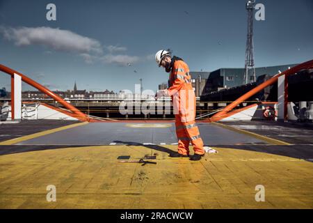 Young offshore engineer manual sounding fuel oil cargo tank on cargo deck on supply vessel in harbor. Stock Photo