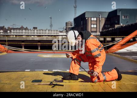 Young offshore engineer sounding fuel oil cargo tank on cargo deck on supply vessel in harbor. Stock Photo