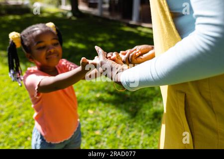 Midsection of african american mother holding daughter's hands in backyard on sunny day Stock Photo