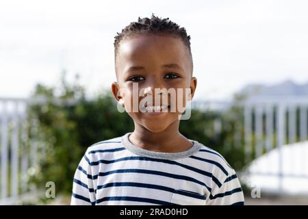 Portrait of cute african american boy smiling at camera while standing against clear sky in yard Stock Photo