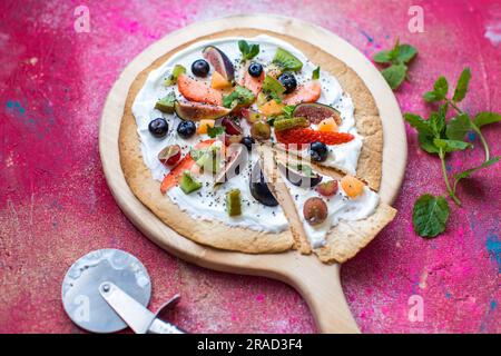 Fruit Pizza made from a toasted Tortilla wrap base, with natural yogurt, fresh fruit toppings, chia seeds and mint to garnish Stock Photo