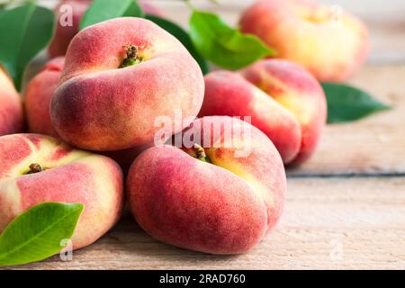 Fresh peaches with leaves on wooden background. Doughnut or vineyard type of flat peach. Stock Photo