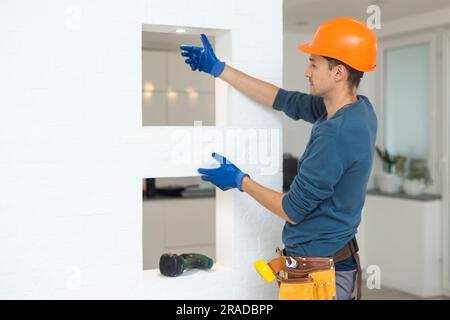 Handsome young builder in construction helmet is twisting the light bulb in. The man is looking up. Stock Photo