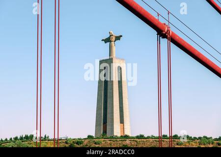 Christ the King, Cristo Rei statue in Lisbon, Portugal. Jesus Christ monument as seen from 25 de Abril Bridge, 25th of April suspension Bridge. Stock Photo