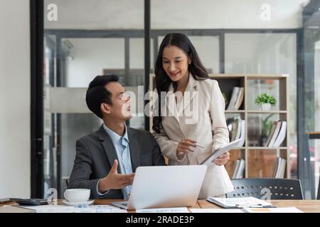 Two happy business women and man, office employees work in office, share creative ideas, feel satisfied with corporation, engaged in teamwork Stock Photo