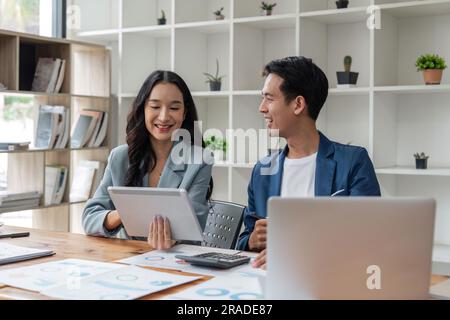 Two happy business women and man, office employees work in office, share creative ideas, feel satisfied with corporation, engaged in teamwork Stock Photo
