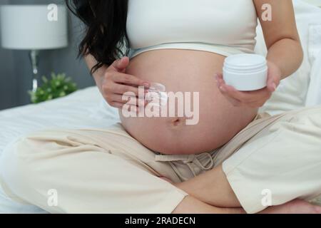close up pregnant woman stroking apply cream on her belly for beauty moisturizing skin on a bed Stock Photo