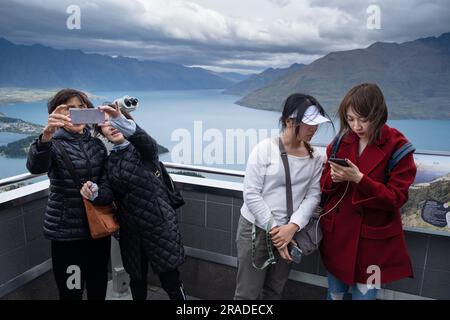 Asian tourists take mobile phone pictures at the Skyline Resort on Bob's Peak above Queenstown and Lake Wakatipu in New Zealand. Photo: Rob Watkins Stock Photo