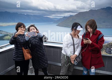 Asian tourists take mobile phone pictures at the Skyline Resort on Bob's Peak above Queenstown and Lake Wakatipu in New Zealand. Photo: Rob Watkins Stock Photo
