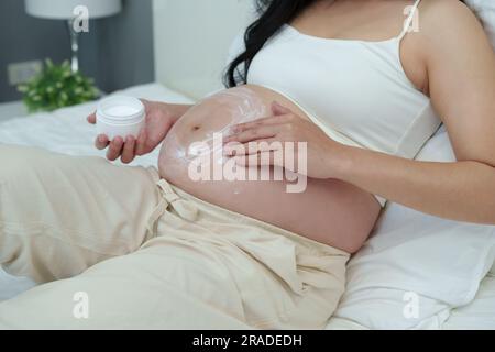 close up pregnant woman stroking apply cream on her belly for beauty moisturizing skin on a bed Stock Photo
