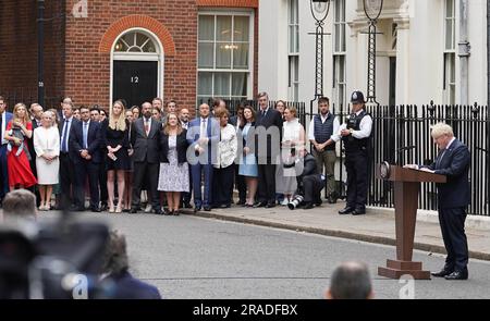 Prime Minister Boris Johnson, watched by wife Carrie Johnson (far left holding daughter Romy) and Charlotte Owen (front row 5th left) , reads a statement outside 10 Downing Street, London, formally resigning as Conservative Party leader after ministers and MPs made clear his position was untenable. He will remain as Prime Minister until a successor is in place. Picture date: Thursday July 7, 2022. Stock Photo