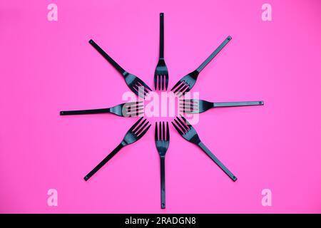Top view composition of black plastic forks placed on pink background Stock Photo