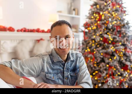 Head shot web camera view happy young handsome man with decorated festive tree on background holding video call, greeting with Happy New year or Merry Stock Photo