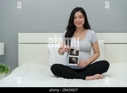 happy pregnant woman looking ultrasound photo of baby on a bed Stock Photo